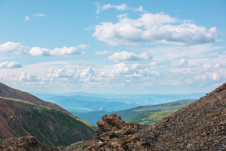 Scenic landscape with sunlit stone outliers with view to mountain vastness under cloudy sky. Colorful mountain scenery with sharp rocks on mountain pass under clouds in blue sky at changeable weather.の写真素材