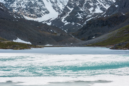 Atmospheric landscape with frozen lake surface and high snowy mountains with light and shadows. Awesome mountain scenery with icy texture of frozen alpine lake. Ice lake among large snow mountains.の写真素材