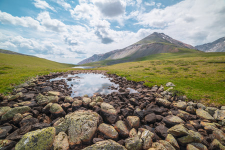 Scenic alpine landscape with two mountain lakes in sunlit mountain valley under cloudy sky. Dramatic sunny scenery with clouds reflection in water mirror of small lake among lichen stones in sunlight.の写真素材