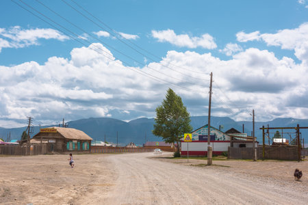 Dramatic landscape inside beautiful mountain village against large mountains at changeable weather. Little girl runs across street. Child crosses road. Russia, Altai Republic, Kurai, 13 July, 2021.のeditorial素材