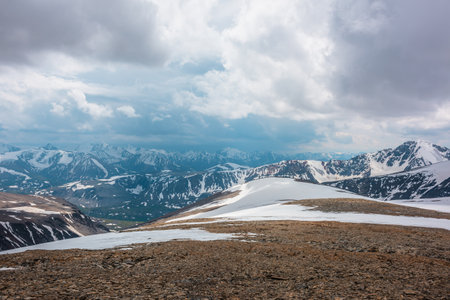 Awesome alpine scenery with snow mountains under cloudy sky. Scenic mountain landscape at very high altitude in overcast. Beautiful atmospheric view from stone hill with snow to snowy mountain range.の写真素材