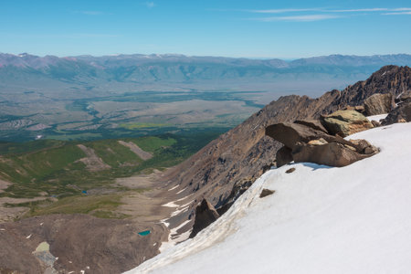Scenic mountain landscape with sharp rocks among snow near abyss to very high altitude. Awesome vertigo view from precipice edge with snow cornice to large mountain range under blue sky in sunny day.の写真素材