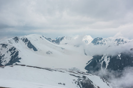 Awesome aerial view to high snowy mountain and dense low clouds. Minimalist alpine landscape with beautiful mountain peaks in thick clouds. Simple minimalism with snow mountain tops under cloudy sky.の写真素材