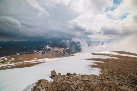 Awesome top view through clouds to high snowy mountains. Scenic landscape with beautiful snow mountains in low clouds. Atmospheric alpine view from stone hill to snow mountain range with low clouds.の写真素材