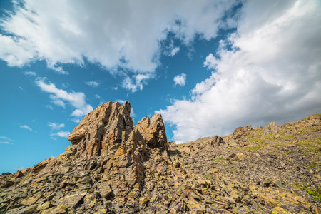 Scenic mountain landscape with stone outliers on rocky hill in sunlight under cloudy sky. Colorful scenery with sunlit sharp rocks on stone mountain under clouds in blue sky at changeable weather.の写真素材