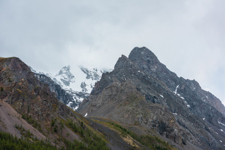 Atmospheric mountain landscape with large pointy pinnacle under gray cloudy sky. Gloomy scenery with high pointed mountain peak with sharp rocks in low clouds. Huge rocky peaked top in rainy weather.の写真素材