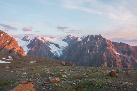 Vivid alpine landscape with high snow mountains and large glacier in sunrise colors. Colorful mountain scenery with sunlit pink rocks and gold mountains at sunrise. Early morning at very high altitudeの写真素材
