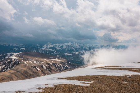 Awesome top view through clouds to high snowy mountains. Scenic landscape with beautiful snow mountains in low clouds. Atmospheric alpine view from stone hill to snow mountain range with low clouds.の写真素材