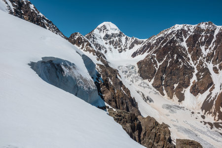 Scenic alpine landscape with snow-covered mountain top and steep glacier tongue with icefall in sunlight. Awesome mountain scenery with pointed peak and glacier on rocks under blue sky in sunny day.の写真素材