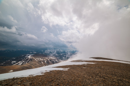 Awesome top view through clouds to high snowy mountains. Scenic landscape with beautiful snow mountains in low clouds. Atmospheric alpine view from stone hill to snow mountain range with low clouds.の写真素材