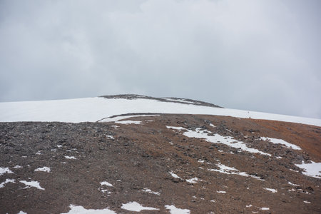 Dramatic landscape with huge rock mountain with snowy mountain dome under gray cloudy sky. Awesome scenery with high snow mountain in dome shape in center at overcast weather. Dome shaped mountain topの写真素材