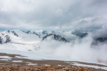 Awesome aerial view to high snowy mountains in dense low clouds. Minimal landscape with beautiful mountain peaks in thick clouds. Simple minimalism with snow mountain tops in cloudy sky above clouds.の写真素材
