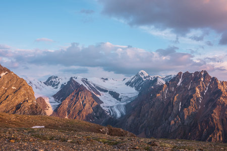 Vivid alpine landscape with high snow mountains and large glacier in sunrise colors. Colorful mountain scenery with sunlit golden rocks and mountains at sunrise. Early morning at very high altitude.の写真素材