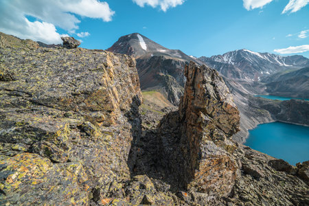 Scenic landscape with sunlit stone outliers with view to two mountain lakes and snow mountains in bright sun. Colorful scenery with sharp rocks and alpine lakes under clouds in blue sky at sunny day.の写真素材