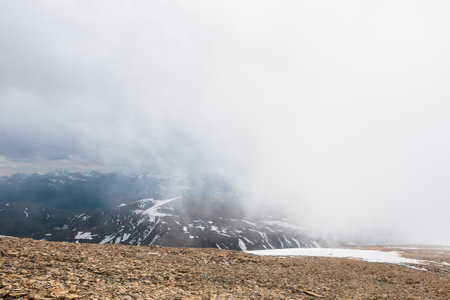 Awesome top view through clouds to high snowy mountains. Scenic landscape with beautiful snow mountains in low clouds. Atmospheric alpine view from stone hill to snow mountain range with low clouds.の写真素材