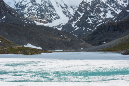 Atmospheric landscape with frozen lake surface and high snowy mountains with light and shadows. Awesome mountain scenery with icy texture of frozen alpine lake. Ice lake among large snow mountains.の写真素材
