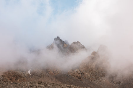 Scenic alpine landscape with rocky mountains in dense low clouds in morning sunlight. Colorful mountain scenery with sharp rocks among thick low clouds. Awesome view to high rockies in low cloudiness.の写真素材