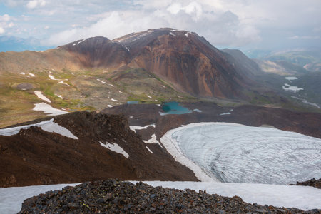 Dramatic landscape with contrast between sunny and rainy weather. Awesome scenery with sharp rocks and small lake in mountain valley. Changeable weather in mountains is sunny and cloudy at same time.の写真素材