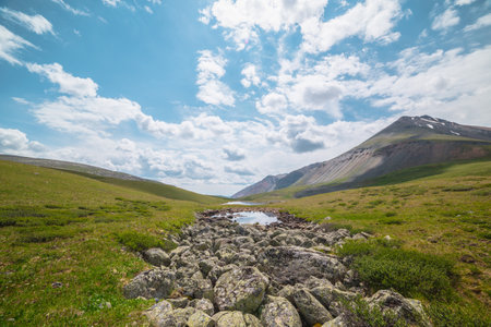 Scenic alpine landscape with two mountain lakes in sunlit mountain valley under cloudy sky. Dramatic sunny scenery with clouds reflection in water mirror of small lake among lichen stones in sunlight.の写真素材
