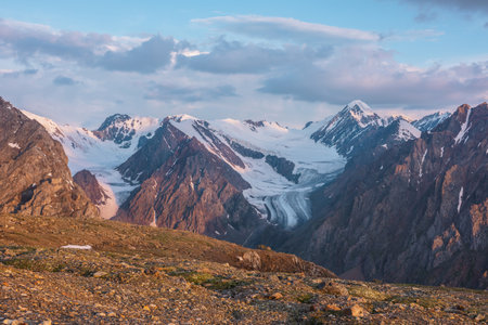 Vivid alpine landscape with high snow mountains and large glacier in sunrise colors. Colorful mountain scenery with sunlit golden rocks and mountains at sunrise. Early morning at very high altitude.の写真素材