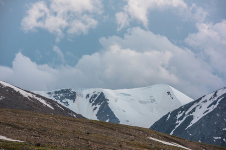 Dramatic landscape with large snowy mountain range under cloudy sky. Awesome alpine scenery with snow mountains under clouds in blue sky at changeable weather. Scenic mountain view at high altitude.の写真素材