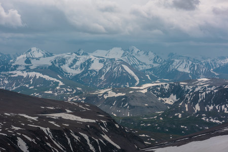 Awesome aerial view to high snow mountains under cloudy sky. Gloomy mountain landscape at very high altitude with cloudiness. Dark atmospheric mountain scenery with snowy mountain range in overcast.の写真素材