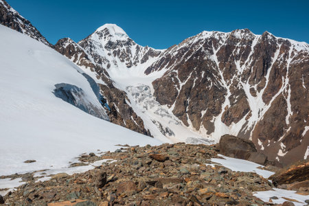 Scenic alpine landscape with snow-covered mountain top and steep glacier tongue with icefall in sunlight. Awesome mountain scenery with pointed peak and glacier on rocks under blue sky in sunny day.の写真素材