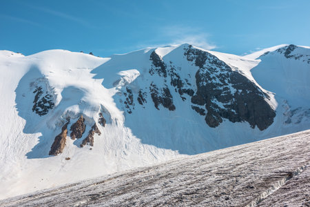 Minimalist mountain landscape with large glacier in sunlight. Simple snowy minimalism with glacial tongue in sunshine. Minimal alpine view to snow mountain tops at very high altitude in sunny day.の写真素材