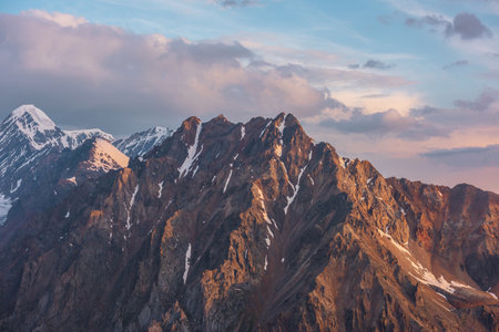 Vivid alpine landscape with high snow rocky pinnacle in gold sunrise colors. Colorful mountain scenery with sunlit golden rocks and snowy mountain peak at sunrise. Early morning at very high altitude.の写真素材