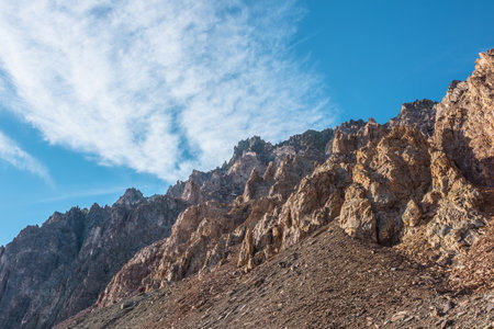 Scenic mountain landscape with sharp rocks under cirrus clouds in sunny day. Colorful scenery with gold sunlit sharp rocky mountains. High rocky mountains in golden sunlight under spindrift clouds.の写真素材