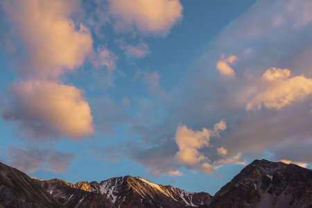 Scenic landscape with high snow mountain with sharp rocky pinnacle in golden sunlight under clouds of sunset color at changeable weather. Colorful view to large mountain top under orange clouds in skyの写真素材