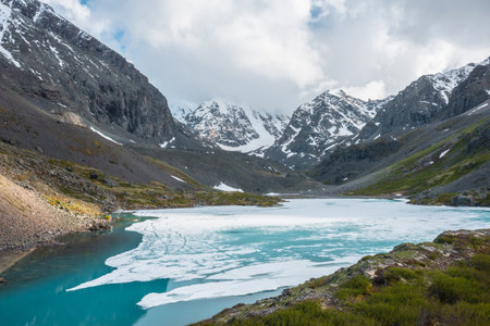 Atmospheric highland landscape with frozen alpine lake and high snowy mountains. Awesome scenery with icy mountain lake on background of large snow mountains in low clouds. Scenic view to ice lake.の写真素材