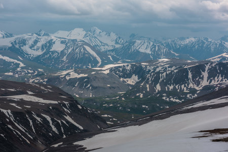 Awesome aerial view to high snow mountains under cloudy sky. Gloomy mountain landscape at very high altitude with cloudiness. Dark atmospheric mountain scenery with snowy mountain range in overcast.の写真素材