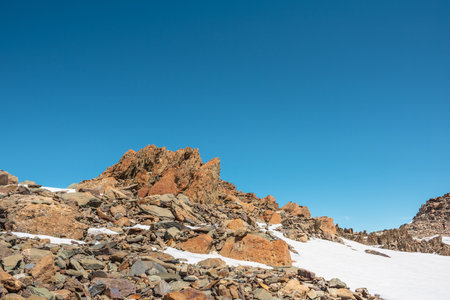 Scenic mountain landscape with old rocks and stones among snow in sunlight. Awesome alpine scenery with stone outliers on high mountain under blue sky in sunny day. Sharp rocks at very high altitude.の写真素材