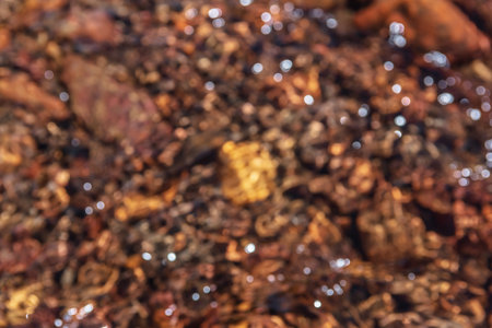 Abstract blur nature background of clear water stream with motley stony bottom in sunlight. Defocused mountain stream texture in bright sun. Blurry pattern of sunlit multicolor stones in spring water.の写真素材