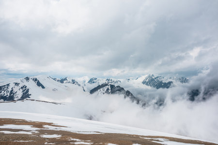 Awesome aerial view to high snowy mountains in dense low clouds. Minimal landscape with beautiful mountain peaks in thick clouds. Simple minimalism with snow mountain tops in cloudy sky above clouds.の写真素材