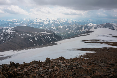 Awesome view from stone hill with sharp stones to snow mountains under cloudy sky. Alpine landscape at very high altitude with cloudiness. Atmospheric scenery with snowy mountain range in overcast.の写真素材