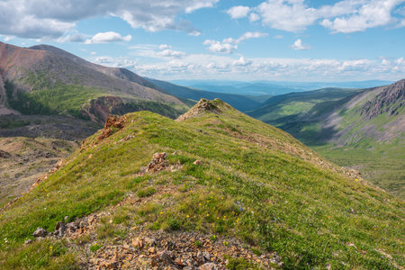 Scenic view from mountain ridge to green forest valley among mountain ranges and hills on horizon at changeable weather. Green landscape with sunlit mountain vastness under cumulus clouds in blue sky.の写真素材