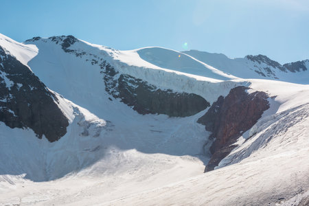 Minimalist mountain landscape with large glacier in sunlight. Simple snowy minimalism with glacial tongue. Minimal alpine view to snow mountain tops at very high altitude under blue sky in sunny day.の写真素材