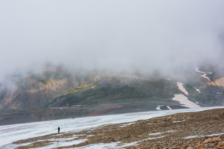Dramatic landscape with people inside cloud above motley mountain valley. Tourists in cloud above multicolor valley. Low cloud on stone hill with snow. Awesome high mountain scenery in low clouds.の写真素材