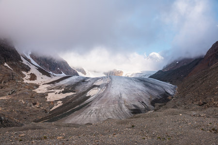 Scenic mountain landscape with large glacier in low clouds in sunrise colors. Colorful view to glacier tongue in morning sunlight in low clouds. Atmospheric high mountain scenery at early morning.の写真素材