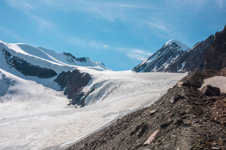 Scenic mountain landscape with large glacier in sunlight. Awesome snowy scenery with glacial tongue under cirrus clouds. Beautiful alpine view to snow mountain tops at very high altitude in sunny day.の写真素材