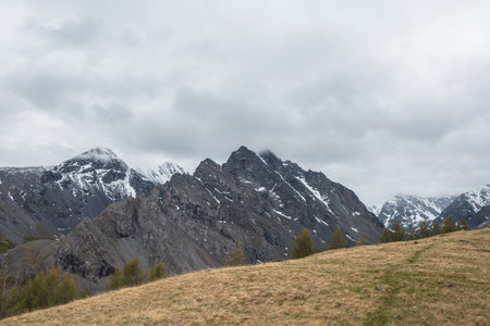 Atmospheric landscape with large thorny dragon shaped mountain top under gray cloudy sky. Gloomy top view from hill to high snowy mountain range with sharp rocks in shape of dragon back in low clouds.の写真素材