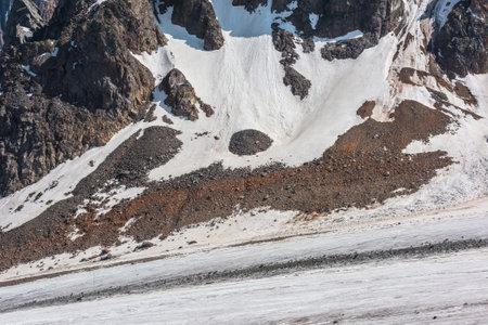 Minimalist mountain landscape with large glacier and rocks with snow in sunlight. Minimal nature background of sunlit glacial tongue and rocky mountains at very high altitude. High mountain minimalismの写真素材