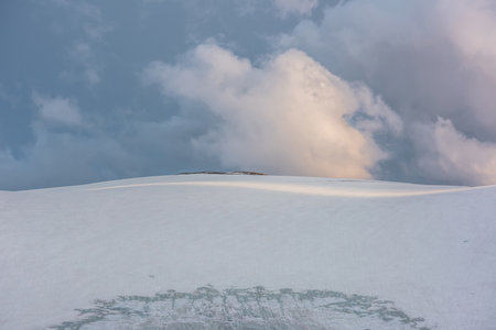 Dramatic landscape with glacier on sunlit high snow mountain top under cloudy sky at sunset. Beautiful alpine landscape with large snowy mountain in sunlight under evening clouds at changeable weatherの写真素材