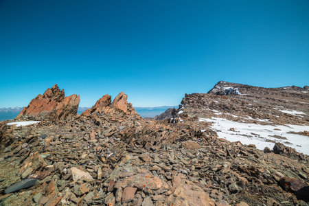 Scenic mountain landscape with old rocks and stones among snow in sunlight. Awesome alpine scenery with stone outliers on high mountain under blue sky in sunny day. Sharp rocks at very high altitude.の写真素材