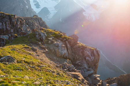 Sunny mountain view from cliff at very high altitude. Scenic alpine landscape with beautiful sharp rocks and couloirs in sunlight. Beautiful scenery on abyss edge with sharp stones and green grass.の写真素材