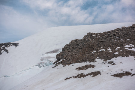 Atmospheric landscape with high snow mountain with sharp rocks under cirrus clouds in blue sky. Beautiful alpine scenery with large snowy mountain under spindrift cloudy sky at changeable weather.の写真素材