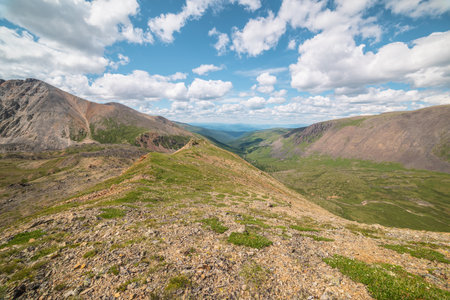 Scenic view from mountain ridge to green forest valley among mountain ranges and hills on horizon at changeable weather. Green landscape with sunlit mountain vastness under cumulus clouds in blue sky.の写真素材