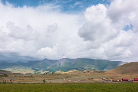 Dramatic alpine landscape with sunlit green high mountain range under gray rainy low clouds. Beautiful mountain scenery with contrast of light and shadow in changeable weather. Overcast in mountains.の写真素材